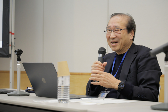 Dr. Kitagawa smiling while holding a microphone at a desk