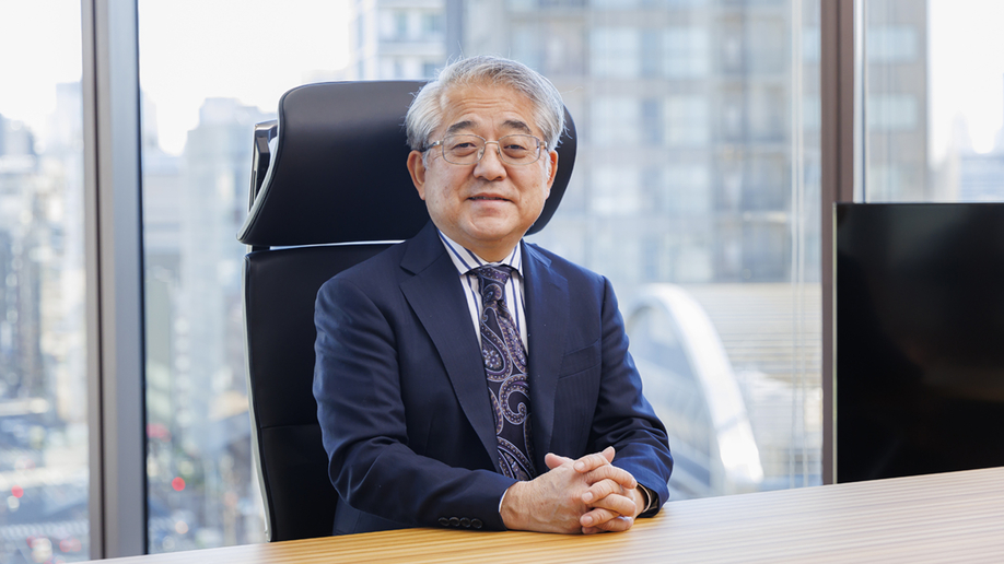 理事長室の椅子に座って笑顔を向ける杉野理事長