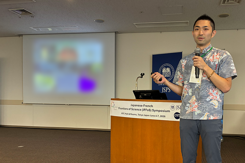 発表者がスクリーン前でマイクを持ち講演している様子