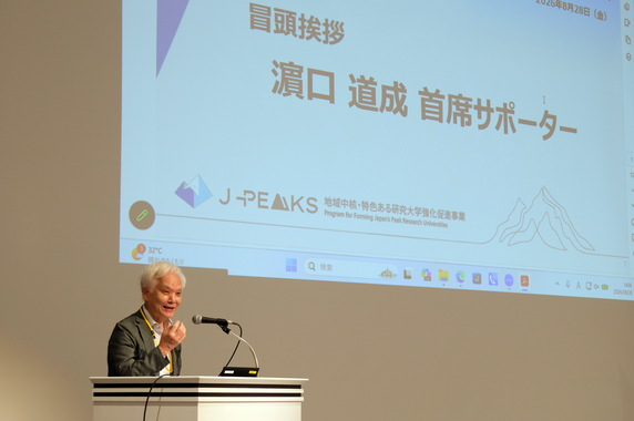 Dr. HAMAGUCHI speaking with a screen in the background.